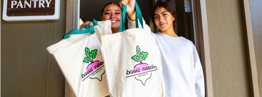 3 of 4, Two staff members holding Basic Needs branded bags 